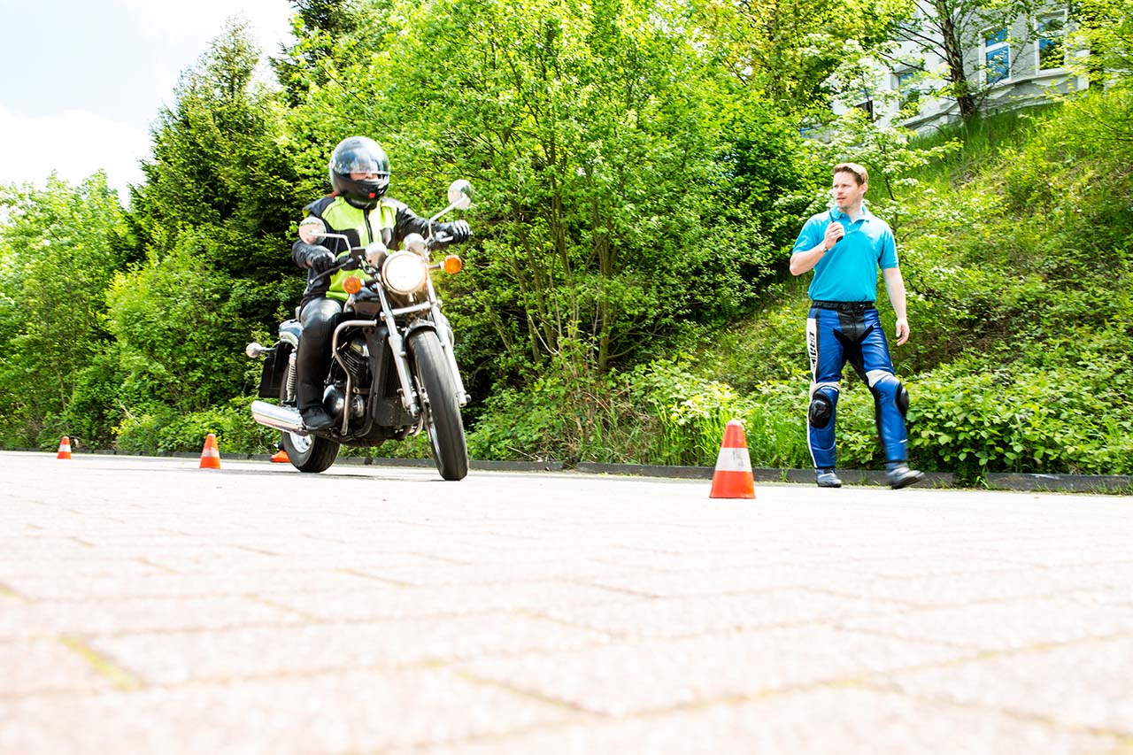 driving instructor and student on a motorcycle with traffic cones